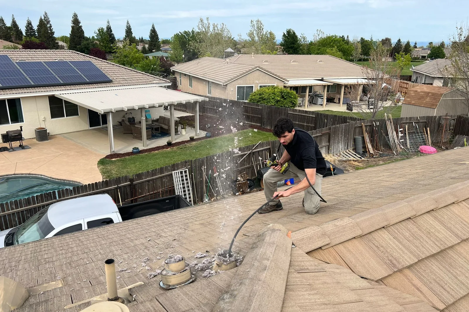 A Chimney Guys technician clearing a rooftop dryer vent, lint blowing clear of the duct