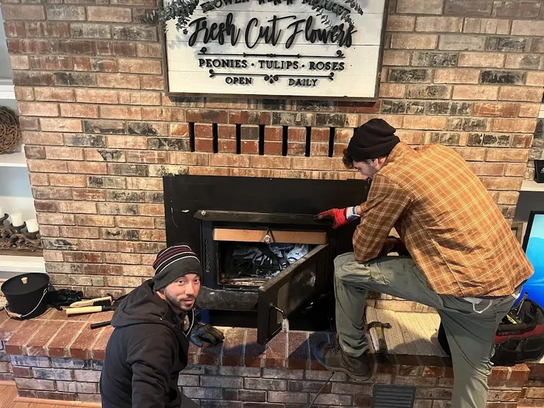 Two Chimney Guys technicians working together on a brick firebox, tools laid out on the hearth